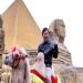 Un touriste chinois se fait photographier  dos de chameau devant une pyramide gyptienne dans un parc d